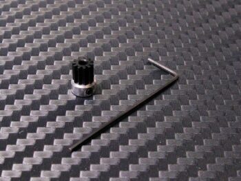 De afbeelding toont een zwart tandwiel met een zilverkleurige basis en een inbussleutel. Het geheel ligt op een donkere ondergrond met een geweven patroon.