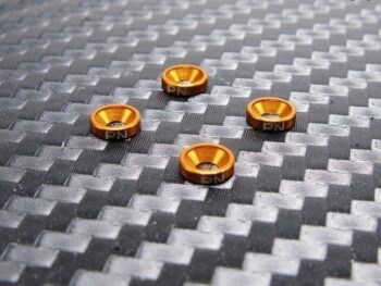 De afbeelding toont vier oranje, metalen ringen met een verzonken gat in het midden. Op de zijkant van elke ring staat 'PN' gegraveerd.