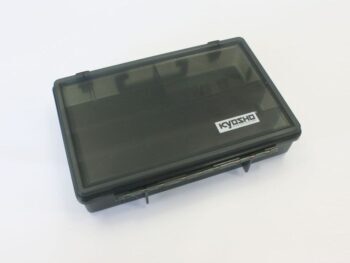 De foto toont een rechthoekige, donkergrijze tot zwarte opbergdoos van plastic met een transparant deksel. Op het deksel is een wit logo van 'KYOSHO' zichtbaar.