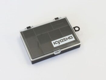 La photo montre une boîte de rangement rectangulaire noire avec un couvercle transparent. Le mot « KYOSHO » est imprimé en lettres blanches sur le couvercle.