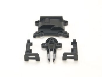 Op de foto zijn vier zwarte plastic onderdelen te zien, waaronder een groter rechthoekig onderdeel en drie kleinere, meer complexe onderdelen die mogelijk dienen als houders of clips.