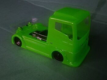 De afbeelding toont een felgroene, glimmende lexaan bodykit voor een mini-truck, bestaande uit een cabine en een gestroomlijnd chassis. De body is ongeschilderd en heeft een transparante achtervleugel.