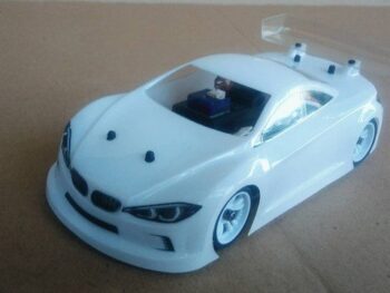 De foto toont een witte, ongeschilderde lexan carrosserie voor een RC-auto, met een transparante achterspoiler. De carrosserie heeft de vorm van een sportieve auto met details zoals koplampen en een grille.