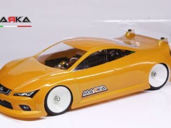De foto toont een oranje gekleurde auto body voor een modelauto, met een transparante vleugel. De body heeft witte wielen en het merk 'MARKA' is zichtbaar.
