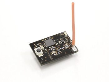 De foto toont een kleine, rechthoekige zwarte printplaat met diverse elektronische componenten en een oranje/roze antenne die eruit steekt. Er is een kleine grijze knop zichtbaar aan de linkerkant van de printplaat.