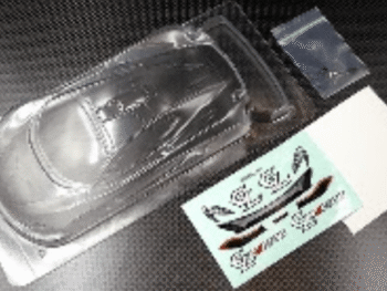Op de foto zie ik een doorzichtige lexan body voor een modelauto, verpakt in plastic. Er zitten ook stickers en kleine onderdelen bij.