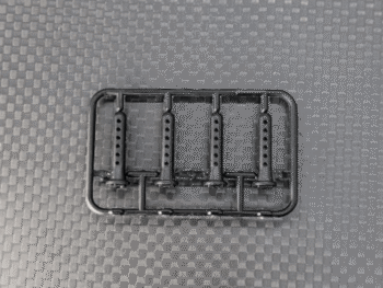 Op de foto is een zwart plastic frame te zien met daarin vier identieke, langwerpige onderdelen met meerdere kleine gaatjes. Het geheel ligt op een donkergrijze, geweven ondergrond.