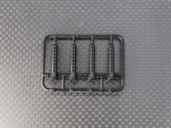 Op de foto is een zwart plastic frame te zien met daarin vier identieke, langwerpige onderdelen met meerdere kleine gaatjes. Het geheel ligt op een donkergrijze ondergrond met een ruitpatroon.