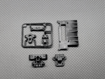 De afbeelding toont diverse zwarte kunststof onderdelen voor een RC auto, waaronder een spruw met kleine onderdelen, een groter chassisdeel en twee kleinere, losse onderdelen. Ze zijn allemaal donker van kleur en lijken van plastic te zijn.