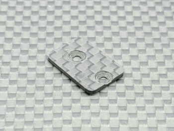 Op de foto is een rechthoekig, grijs carbon onderdeel te zien met twee ronde openingen. Het heeft een geweven patroon dat kenmerkend is voor carbonfiber.