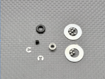 De afbeelding toont een set kleine, metalen en rubberen onderdelen op een grijze, geruite achtergrond. De onderdelen omvatten twee zilverkleurige ringen met kleine metalen balletjes, een zwart rubberen ring, een klein zwart schroefje, twee zilverkleurige C-vormige clips en een klein zilverkleurig lager.
