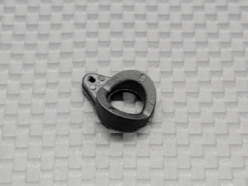 Op de foto is een klein, zwart, ringvormig onderdeel te zien met een platte basis en een uitstekend lipje met twee gaatjes. Het lijkt gemaakt van kunststof of rubber.