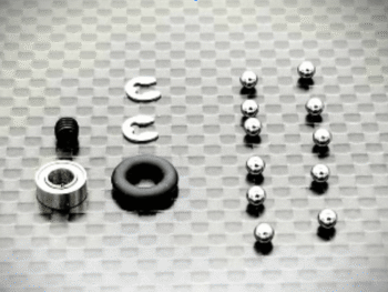De afbeelding toont diverse kleine onderdelen voor een differentieel, waaronder zilverkleurige kogellagers, een zwarte O-ring, twee zilverkleurige C-clips en een zwarte schroef. De onderdelen liggen verspreid op een geruit oppervlak.