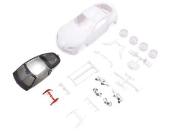 De afbeelding toont een bouwpakket van een witte carrosserie voor een modelauto, met diverse losse onderdelen zoals wielen, een donker getinte ruitenset en andere kleine witte plastic onderdelen. Er is ook een rood, I-vormig onderdeel zichtbaar.