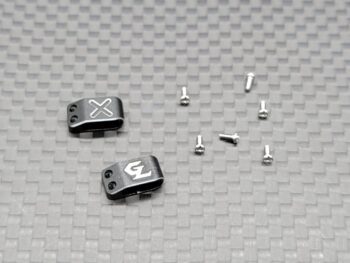 De afbeelding toont twee donkergrijze metalen klemmen met witte logo's ('X' en 'GL') en een aantal kleine zilverkleurige schroefjes. De klemmen hebben elk twee kleine gaatjes aan de zijkant.