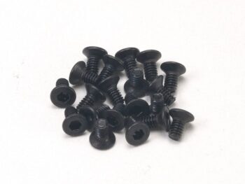 La photo montre un assortiment de vis noires à tête fraisée. Les vis sont dispersées sur un fond blanc.