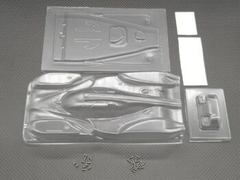 De foto toont een transparante lexan body set voor een RC auto, bestaande uit meerdere voorgevormde onderdelen en twee zakjes met kleine schroefjes. De onderdelen zijn ongeschilderd en hebben een glanzende afwerking.