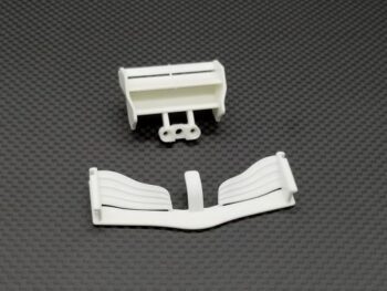 De foto toont twee witte, plastic onderdelen die lijken op een spoiler en een voorvleugel voor een modelauto, liggend op een donkergrijze ondergrond met een koolstofvezelpatroon.