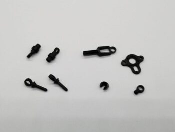 De afbeelding toont een set van kleine, zwarte onderdelen, waarschijnlijk gemaakt van kunststof of metaal. Er zijn verschillende vormen te zien, waaronder pinnen met oogjes, een langwerpig onderdeel met een vierkante opening en een ring, en een onregelmatig gevormd plaatje met gaten.