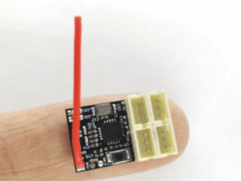 De foto toont een kleine elektronische printplaat met een rode draad die omhoog steekt. Er is ook een witte connector met vier poorten aan de rechterkant van de printplaat.