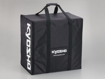 De afbeelding toont een grote, zwarte draagtas van textiel met witte 'KYOSHO' logo's aan de zijkant en voorkant. De tas heeft twee handvatten aan de bovenkant en verticale banden voor extra stevigheid.