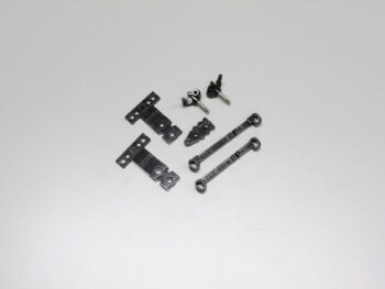 De afbeelding toont een set kleine, donkergrijze tot zwarte onderdelen, waaronder twee T-vormige platen, twee stangen met ogen aan de uiteinden, en enkele kleinere, complexere onderdelen met pinnen. De onderdelen lijken van metaal of hard plastic te zijn.