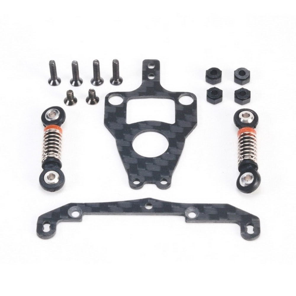 3311g De afbeelding toont een set onderdelen voor een RC-auto, waaronder twee dempers met zilveren veren en oranje accenten, twee zwarte koolstofvezel platen met een geweven patroon, en diverse kleine schroeven en moeren. De onderdelen zijn donkergrijs/zwart met metallic accenten.