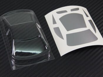 De afbeelding toont een ultradunne, transparante Lexan carrosserie voor een RC auto, samen met een sticker vel met raammaskers. De carrosserie is gevormd naar een GT01 model.