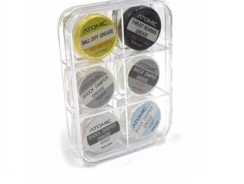 De afbeelding toont een transparante opbergdoos met zes potjes vet voor RC-auto's. De potjes hebben verschillende kleuren labels met merk- en productinformatie.