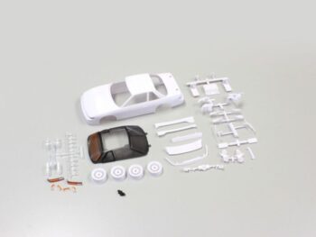 De afbeelding toont een bouwpakket van een witte Nissan Silvia S13 carrosserie voor een Mini-Z modelauto, inclusief een transparant raamdeel en diverse witte onderdelen op een grijze achtergrond.