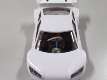 De foto toont een witte spoiler met de tekst 'Mini-zshop.nl' erop, gemonteerd op een witte modelauto. De spoiler heeft een aerodynamische vorm en is gemaakt van kunststof.