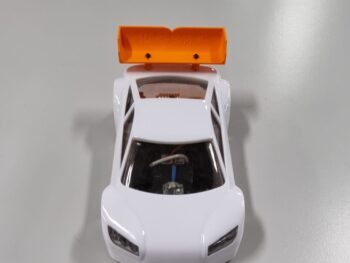 De foto toont een witte modelauto met een feloranje spoiler aan de achterkant. De spoiler heeft de tekst 'Mini-zshop.nl' erop.
