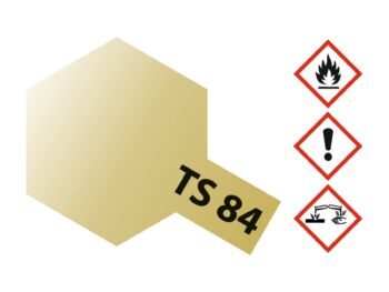 De afbeelding toont een zeshoekig vlak dat van lichtgeel naar goudkleurig verloopt, met een uitstekend rechthoekig label met de tekst 'TS 84'. Rechts staan drie gevaarsymbolen: een vlam, een uitroepteken en een symbool voor corrosie.