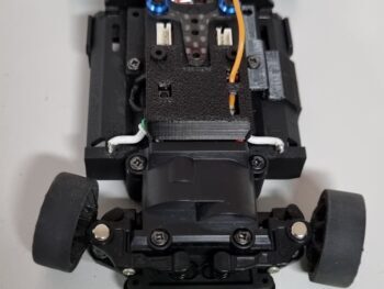 De foto toont een mini-z chassis met een groene bumper en zwarte onderdelen. Er zijn ook wielen en elektronica zichtbaar.