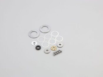 De foto toont een set kleine, ronde metalen onderdelen in verschillende groottes en vormen, waaronder ringen, shims en kogellagers. Er is ook een klein zwart rubberen ringetje en een goudkleurig onderdeel met gaten zichtbaar.