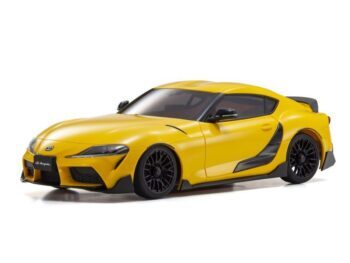 Een gele miniatuur Toyota GR Supra met zwarte accenten en zwarte velgen, afgebeeld op een witte achtergrond. Het is een gedetailleerde carrosserie van een sportwagen.