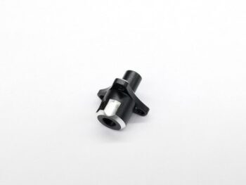 Op de foto is een zwart metalen onderdeel te zien met een cilindrische vorm en uitstekende flenzen. Er is een zilverkleurige rand en een zilverkleurig rechthoekig detail zichtbaar aan één uiteinde.