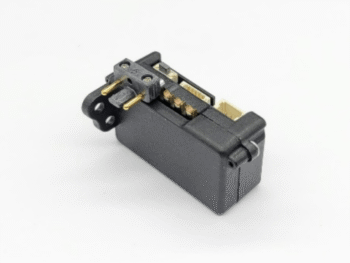L'immagine mostra un componente elettronico compatto di colore nero con connettori dorati e bianchi. Ha una forma rettangolare con dei pin sporgenti su un lato.