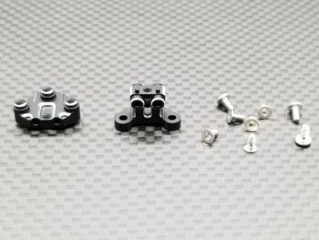 De foto toont twee zwarte metalen onderdelen met diverse gaten en schroefdraad, samen met een aantal zilverkleurige schroeven. De onderdelen lijken precisie-gefreesd te zijn.