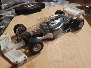 Op de foto is een wit 3D-geprint voorvleugel en een witte achtervleugel te zien, gemonteerd op een transparante carrosserie van een RC-auto. De onderdelen zijn van kunststof en hebben een gestructureerd oppervlak.