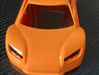 De afbeelding toont een fel oranje, hard plastic carrosserie van een RC-auto. Het product heeft een gestroomlijnde vorm met duidelijke lijnen voor de koplampen en een open dakconstructie.