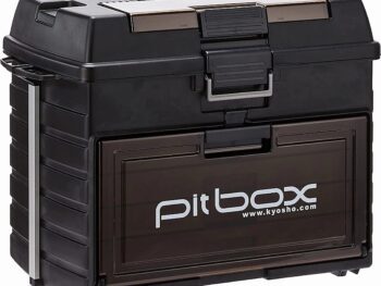 De productafbeelding toont een zwarte transportkoffer met een transparant bruin voorpaneel waarop 'pit box' en 'www.kyosho.com' staat. De koffer heeft metalen accenten en stevige sluitingen.