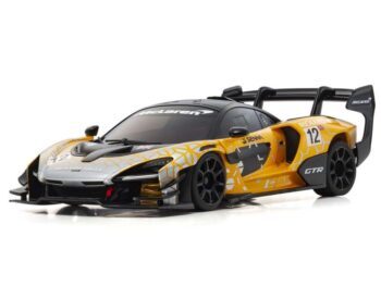 De foto toont een oranje en zilverkleurige modelauto van een McLaren Senna GTR met zwarte details en nummer '12'. Het is een gedetailleerde body van een raceauto.