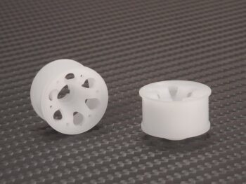La imagen muestra dos llantas de plástico blanco semitransparente con un diseño de seis radios y agujeros en los radios. Se encuentran sobre una superficie gris oscuro con textura.
