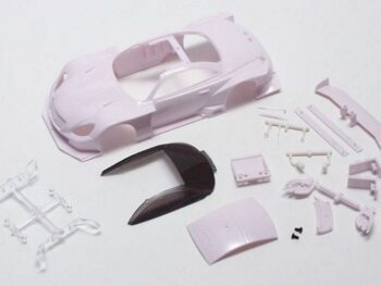 The image shows a model car kit, consisting of a light purple body and various separate parts in the same colour, plus a dark-tinted window and a transparent chassis. The body is shaped like a sports car.