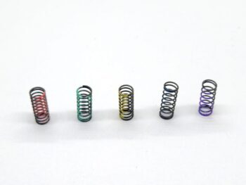 De foto toont vijf kleine, metalen spiraalveren in verschillende kleuren: rood, groen, geel, blauw en paars. Ze liggen naast elkaar op een witte achtergrond.