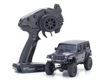 De foto toont een donkergrijze, gedetailleerde miniatuur Jeep Wrangler Rubicon naast een zwarte afstandsbediening. De Jeep heeft een robuust uiterlijk met grote banden en een gedetailleerde grille.