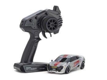 De afbeelding toont een zilverkleurige mini-auto met rode en blauwe strepen, naast een zwarte afstandsbediening. De auto heeft een sportief design met donkere ramen en velgen.