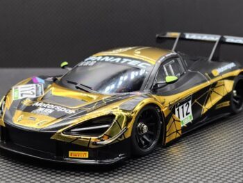 De afbeelding toont een schaalmodel van een McLaren 720S GT3 raceauto. De body is voornamelijk goudkleurig met zwarte accenten en race-graphics.
