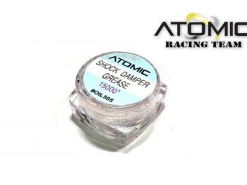 Een klein, transparant, vierkant potje met een lichtblauwe sticker op de deksel. Op de sticker staat 'ATOMIC SHOCK DAMPER GREASE 15000* #OIL505' in zwarte letters. Het potje bevat een transparante substantie.